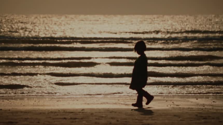 A child walks alone on the beach at sunset