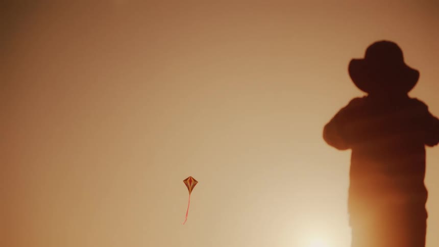 A child is pulling the string while flying a kite at sunrise