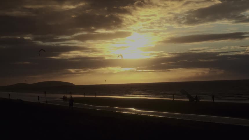 People walk along a serene beach at sunset with a golden sky and gentle ocean waves