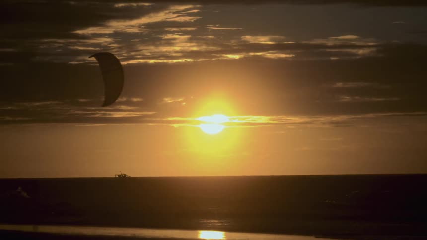 Paraglider gliding across the sky as big yellow sun sets over the horizon
