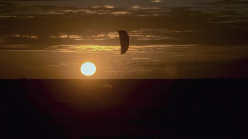 Parachute flying in the middle of the sea with the sun on the horizon