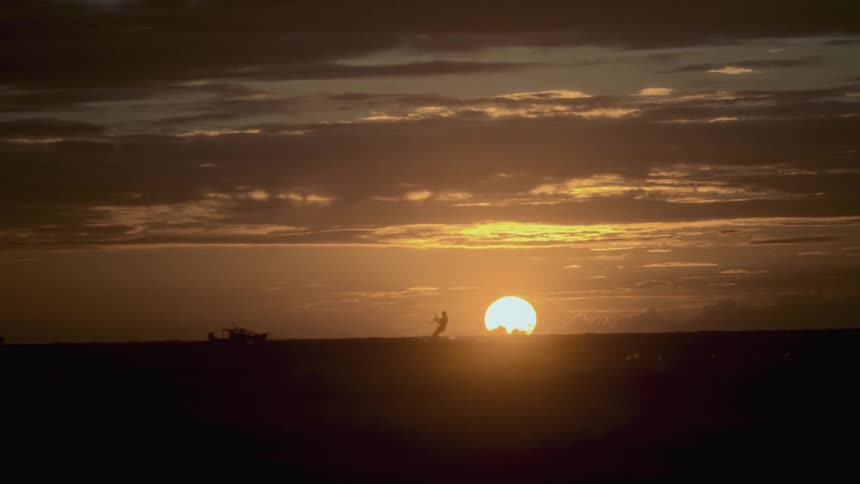 Paraglider gliding across the ocean as big yellow sun sets over the horizon
