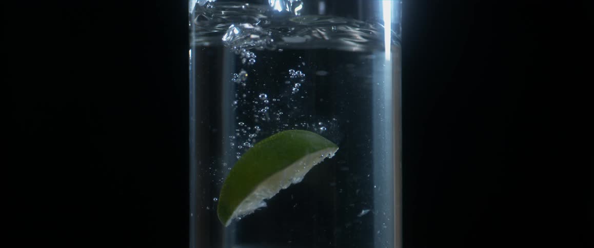 Lemon piece is being dropped into a glass of water