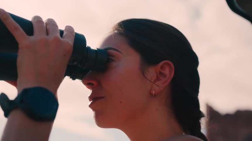 Woman uses a large pair of binoculars while outdoors under an overcast sky