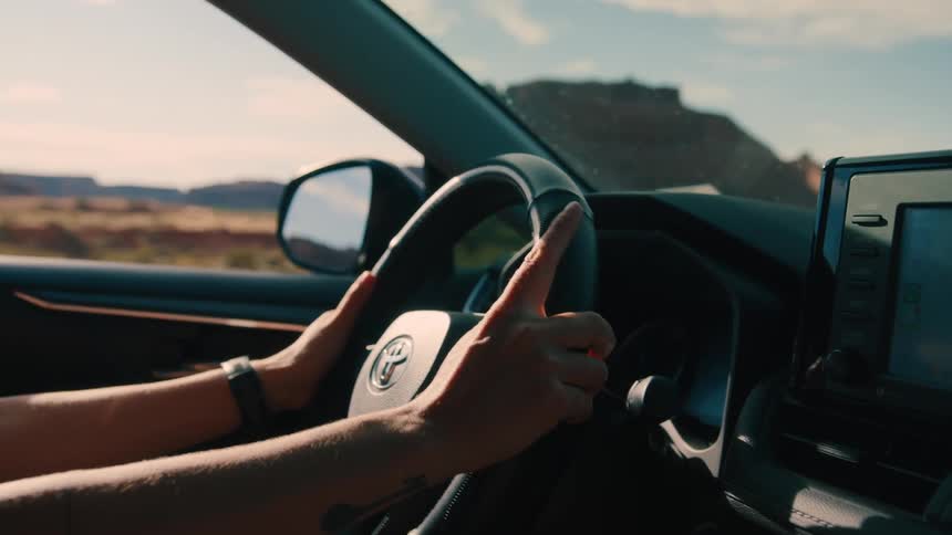 A person drives through the countryside at midday holding the steering wheel with both hands