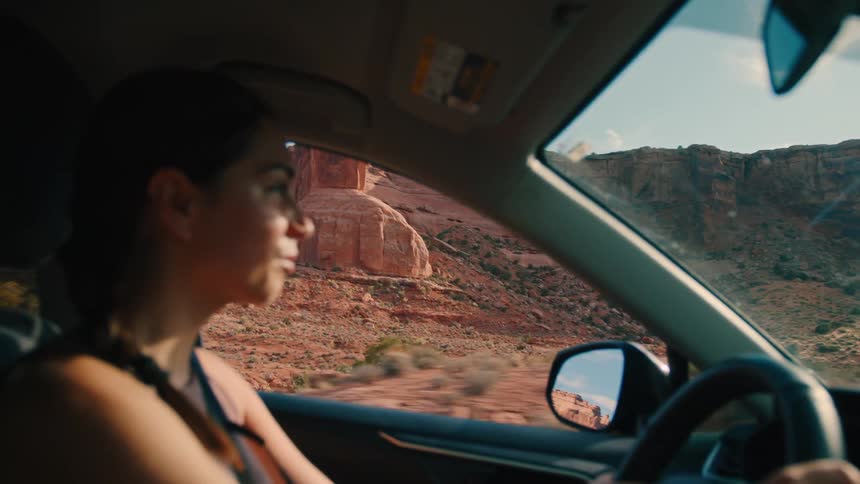 Happy woman driving a car in an area surrounded by canyons