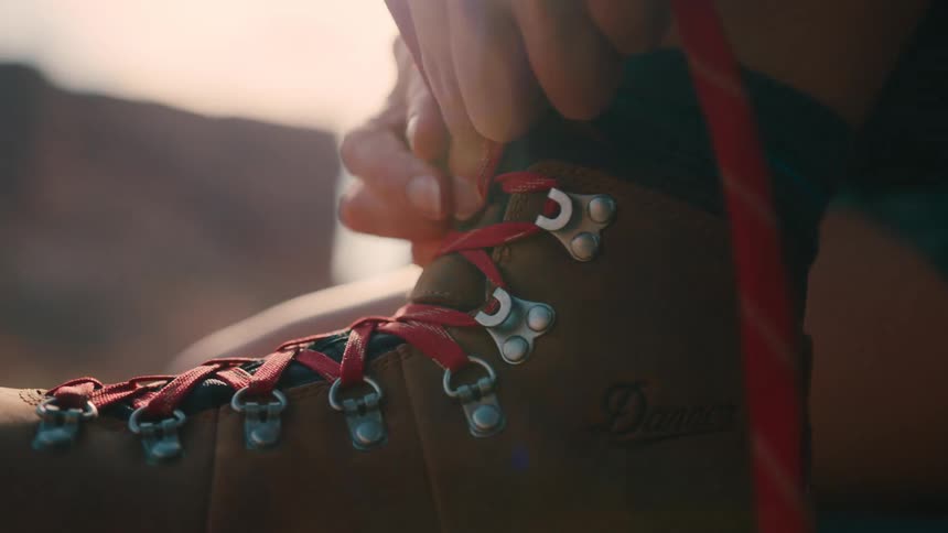 A person ties the shoelaces of their sneakers outdoors at midday