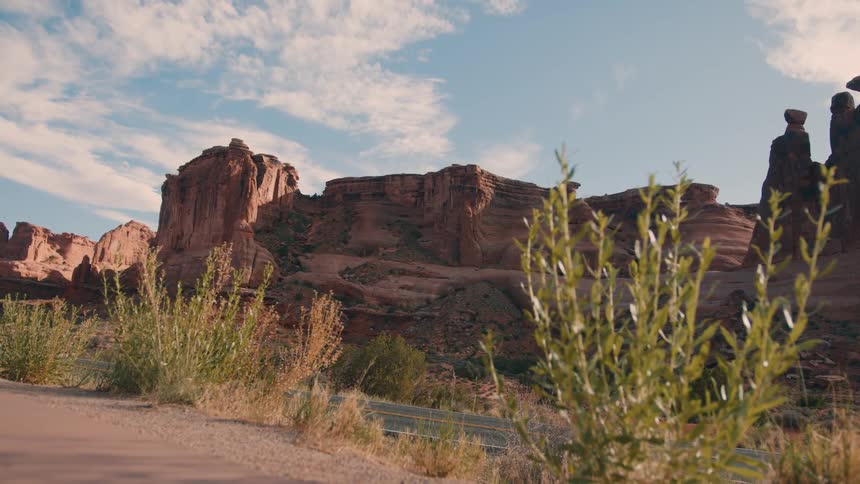 A scenic desert canyon with towering red rock formations and dry plants in the foreground