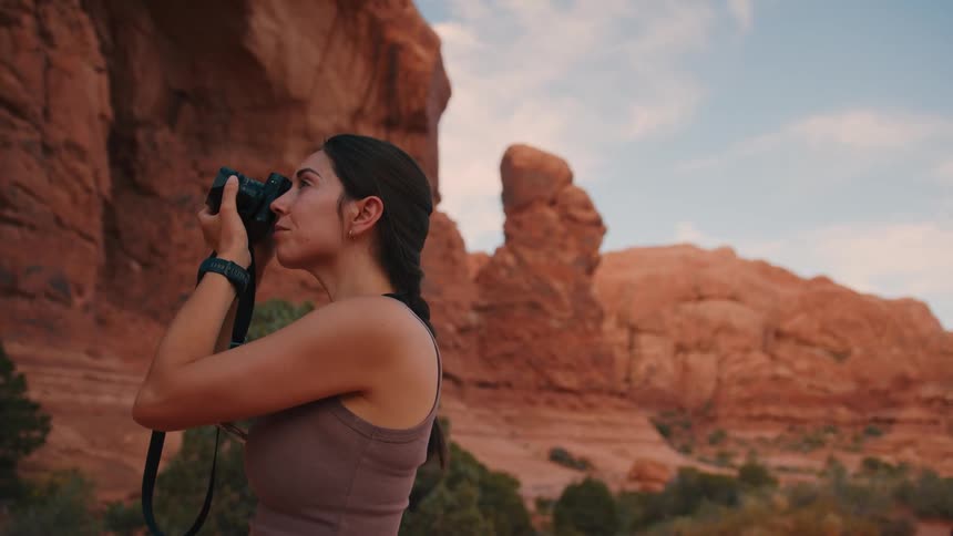 A woman is taking a photo with her camera in a red rock desert landscape during daylight
