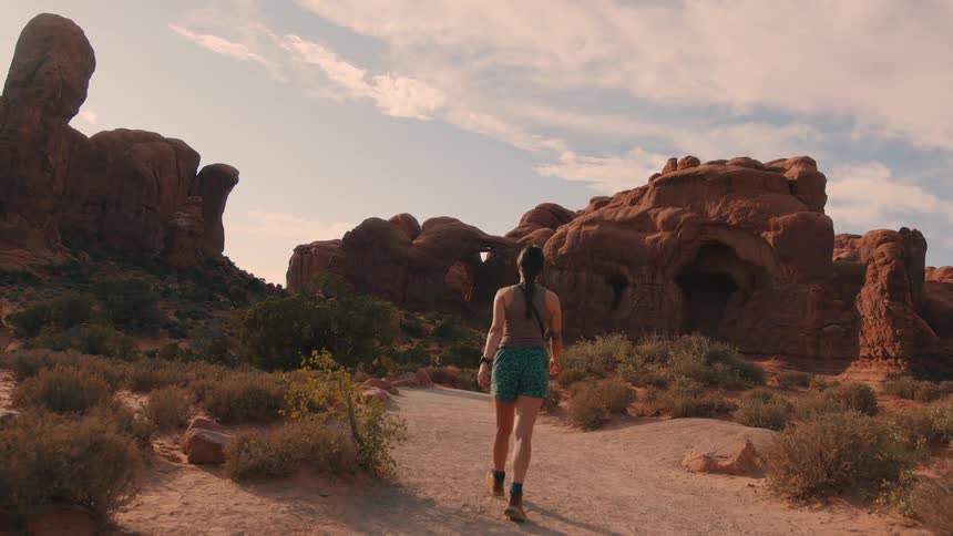 Woman hikes through the arid terrain near multiple rock formations and a cave
