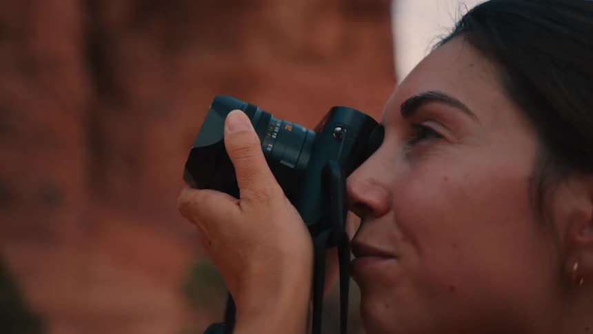 A young woman uses a digital camera to photograph the rocky mountain at midday