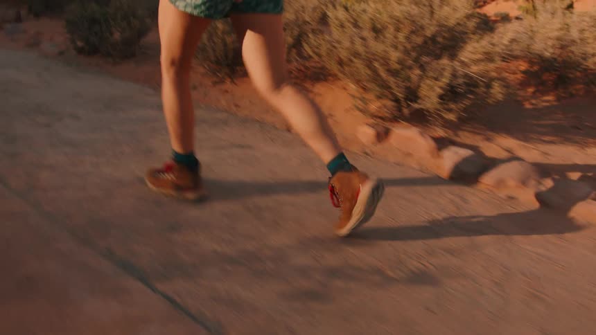 A woman is walking on a path in a desert region and she is wearing brown boots
