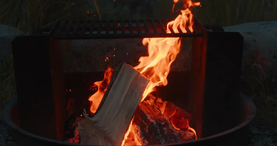 Tree logs are burning in an outdoor bonfire at night