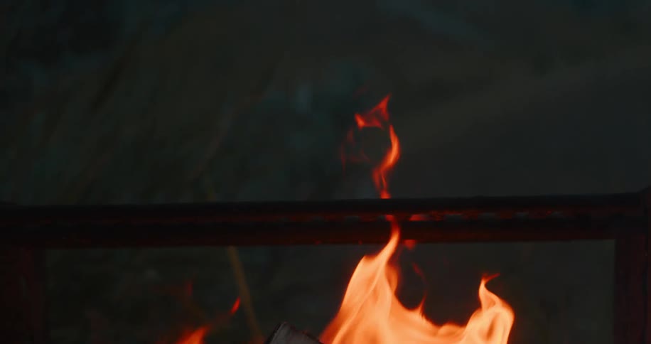 Bright orange flames burn around a log within a metal fire pit with the background visible through the top opening