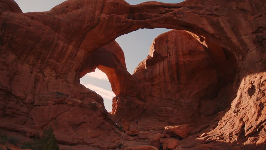 A natural red rock arch formation towers over a rugged desert canyon under a clear sky