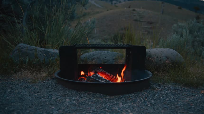 A small campfire burns inside a metal fire ring at a campsite in a natural outdoor setting