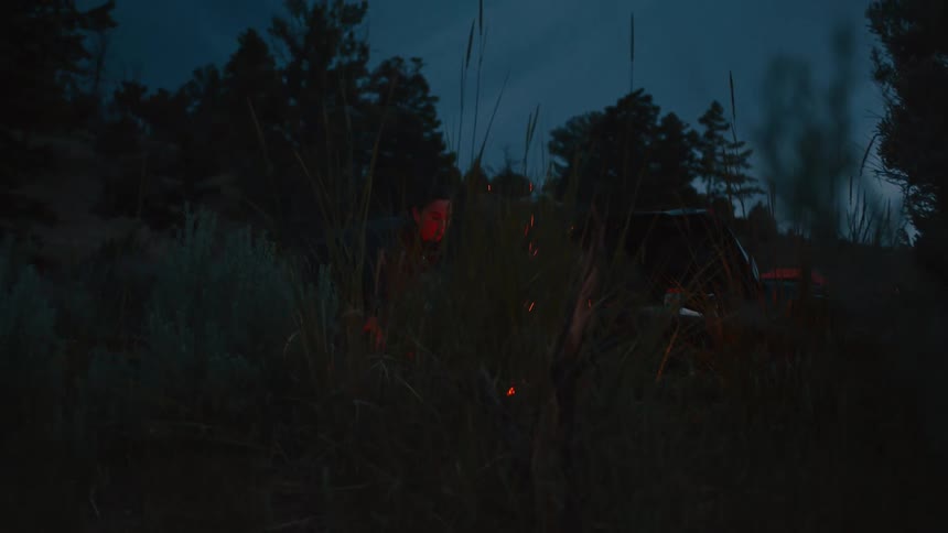 Camper tends to a campfire at dusk