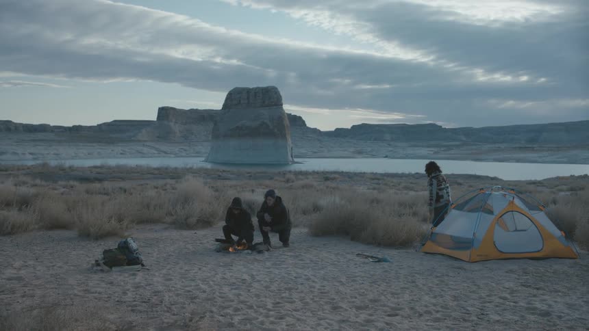Three people walking and sitting by their camp fire