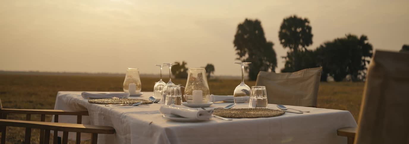 A neatly setup dining table outdoors on a field at sunset