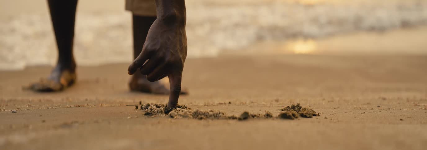 Close up of a black man drawing a circle in the sand at the beach during daytime