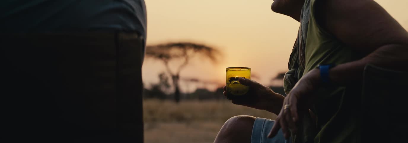 Person sitting holding a glass of drink and talking to another person in front of them