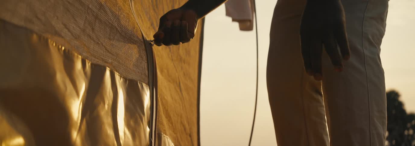 The man is opening the tent zipper