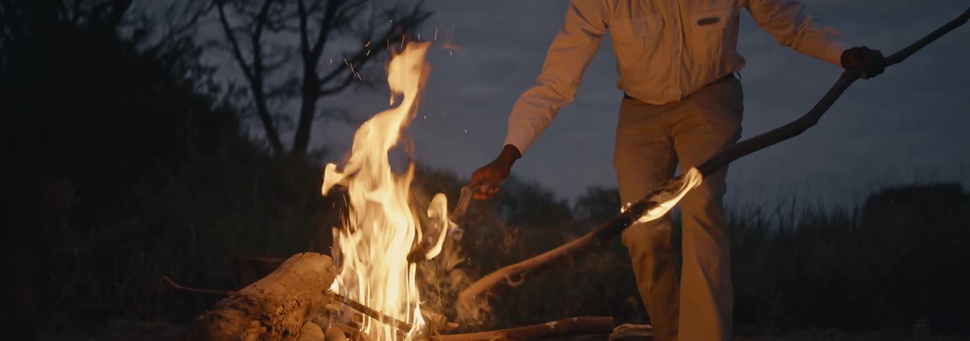 Man adds long pieces of wood to a campfire at night