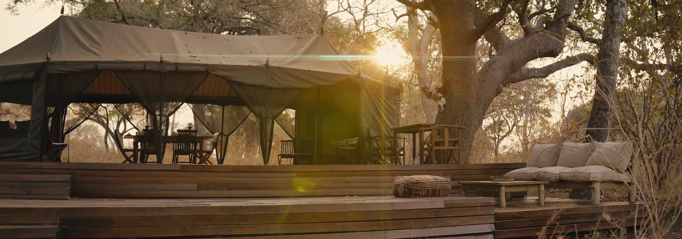 Wooden deck with chairs and sofas in a covered area surrounded by trees