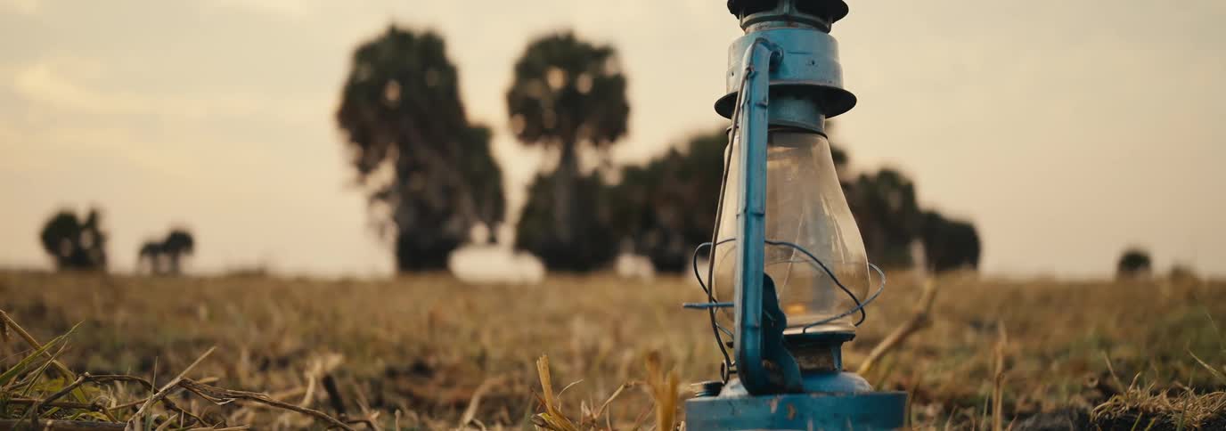 Blue lantern sitting in the dry field with sparse trees far behind it
