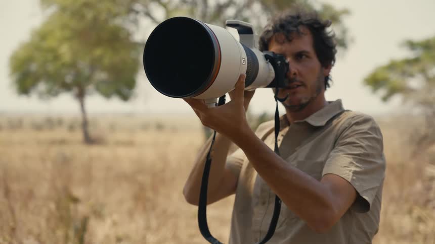 A photographer looks around with a very large lens on a camera