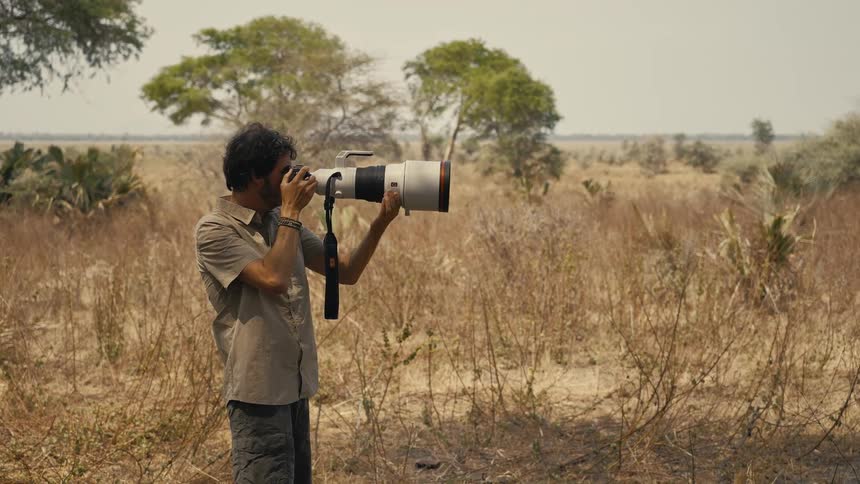 A wildlife photographer shoots with a telephoto lens in a dry grassland