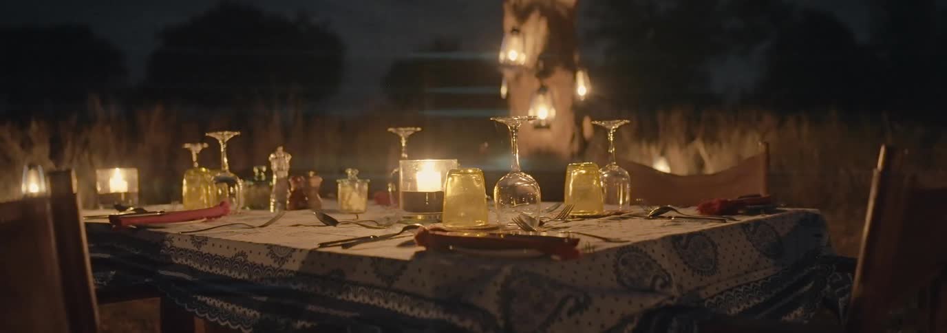 Dining table with glasses and lit candles at night in an outdoor setting
