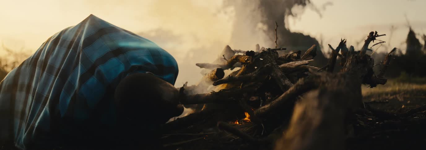 The man blows on the campfire to ignite it