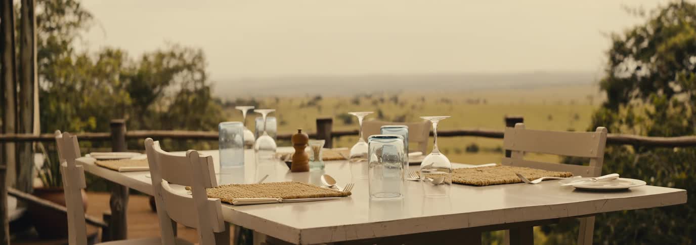 A neatly set outdoor dining table overlooks a vast open savanna landscape