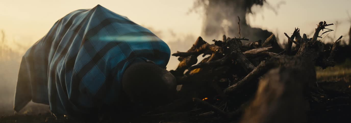 The man is blowing into the campfire to get it started