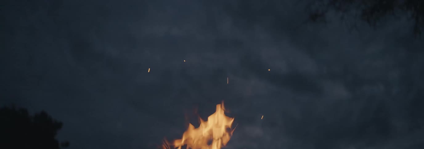 The flame of an igniting orange fire that is throwing some sparks upwards on a night