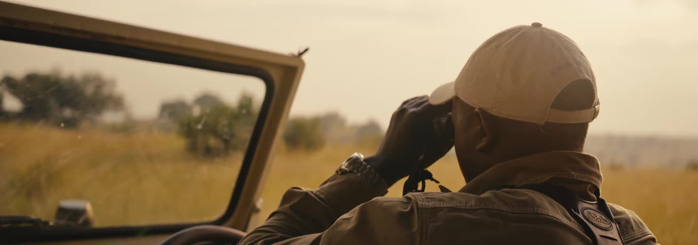 Man sitting in a jeep scans the savanna with binoculars