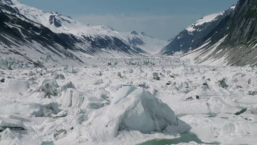 A vast frozen glacier stretches between towering snow covered mountains under a clear sky