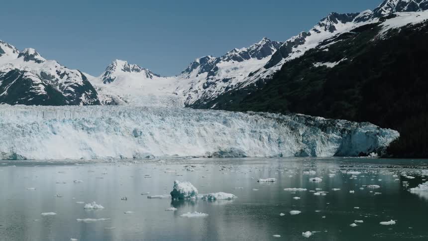 Helicopter aerial in Alaska lake in the arctic with chunks of ice on the surface and icecapped mountains in the background
