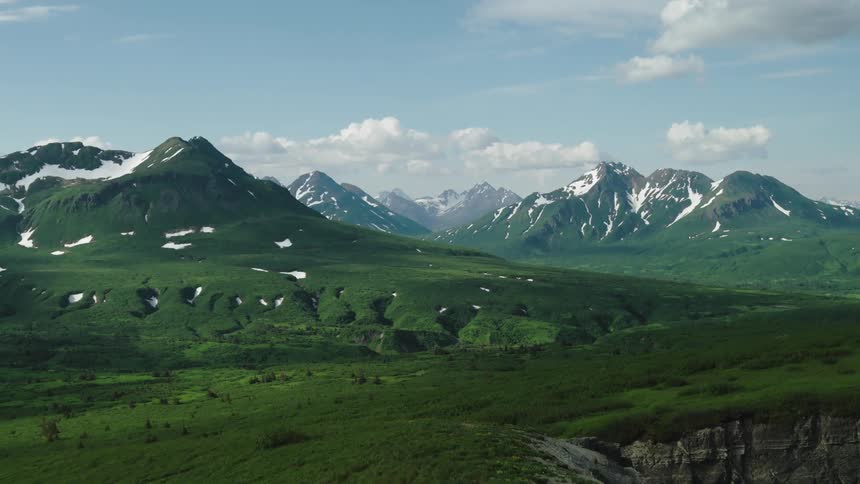 Aerial view of lush green mountains with snow patches under a bright blue sky