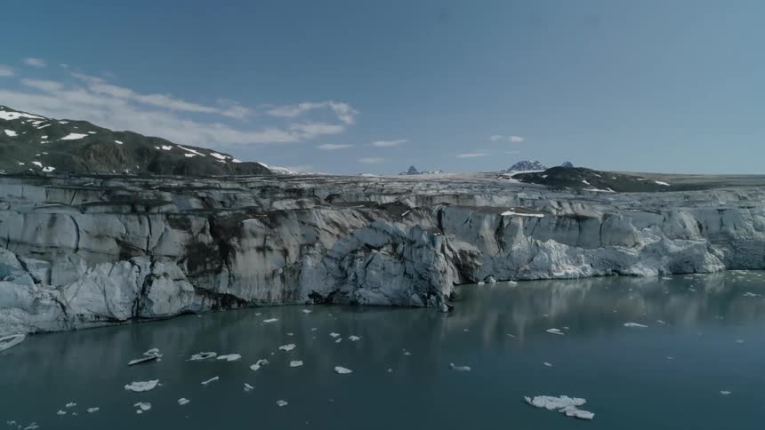 Aerial shot of a rugged arctic glacier cliff meeting icy water