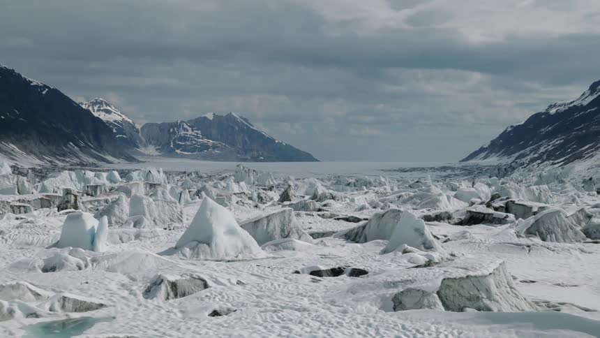 Vast glacier field lies between snowy mountain ranges under a cloudy sky