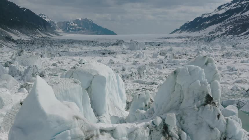 Massive ice sheets span a frozen valley amid snow capped mountains