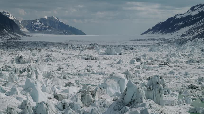 A vast frozen glacier stretches between rugged mountain ranges under a cloudy sky