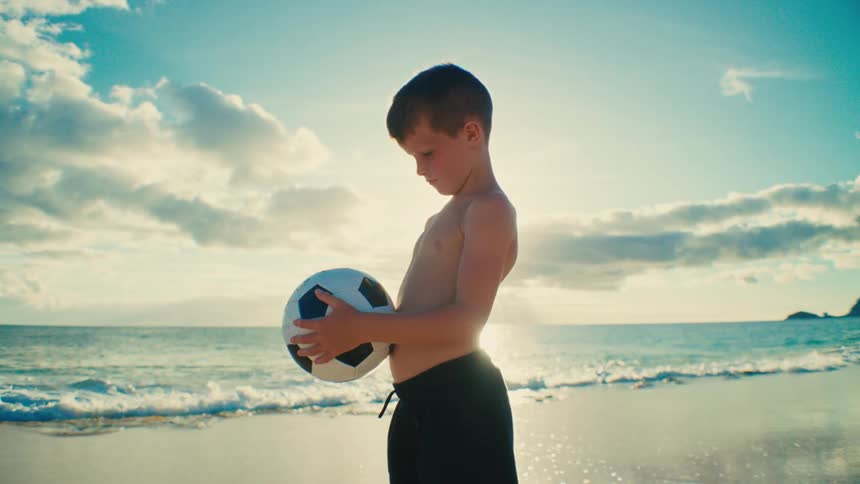 Boy holding a ball while shirtless at the beach