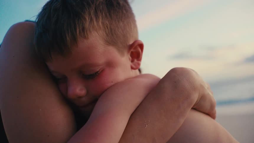 Mother hugs her son while they sit outdoors at the beach during daytime