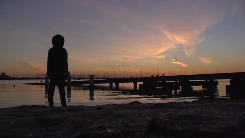 Child stands on beach at sunset