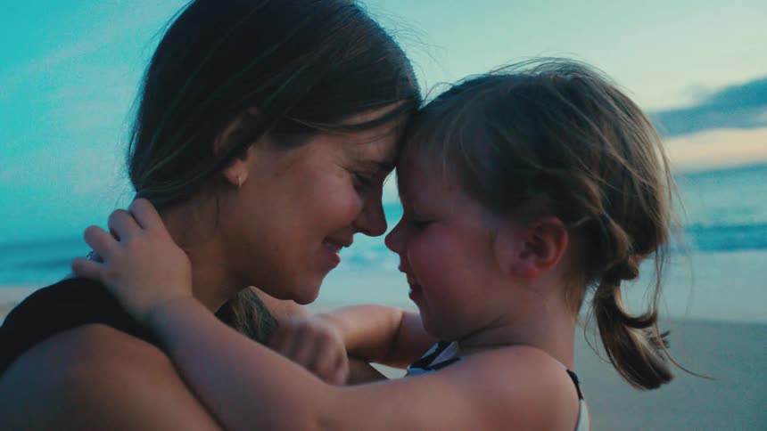 Mother lovingly hugging her little daughter on the beach