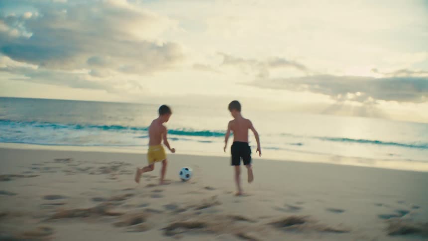Two boys playing soccer on the beach sand