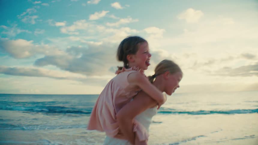 Two sisters play joyfully at the beach one giving a piggyback ride at sunset